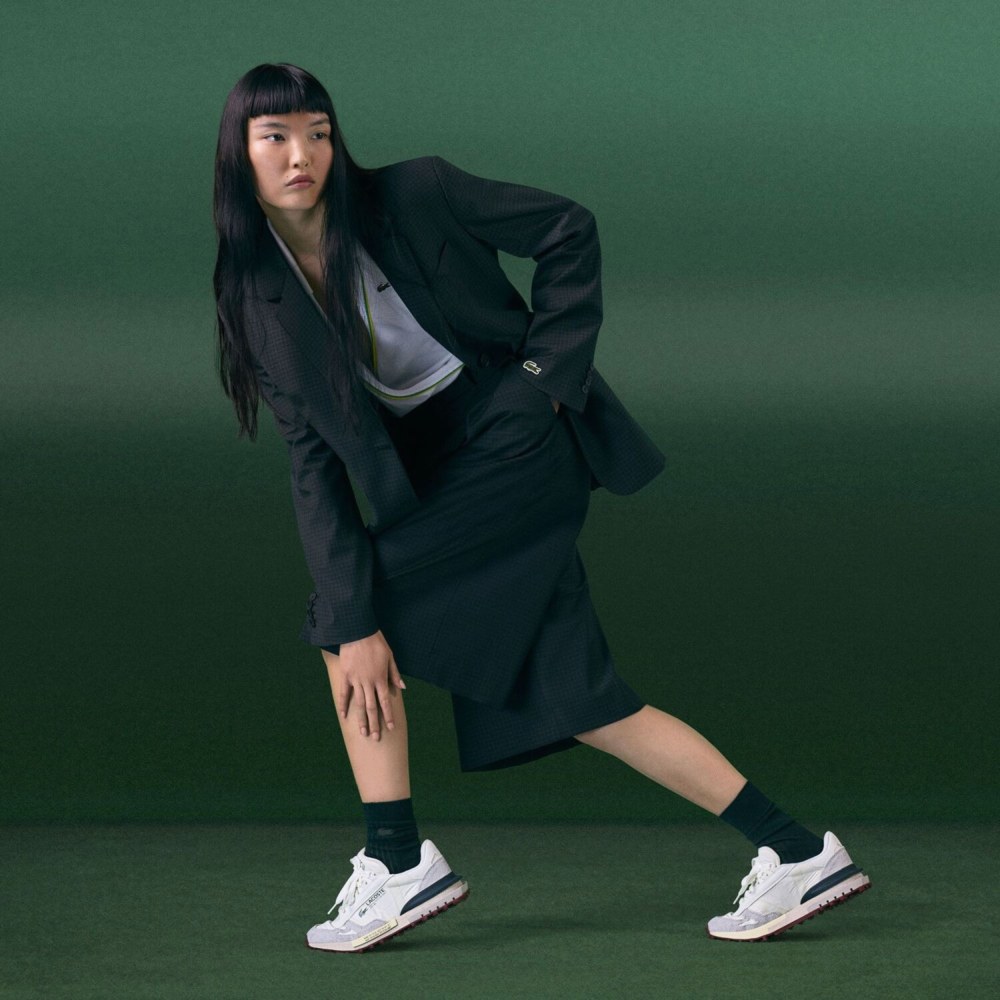 жінка азіатка в темно-зеленій куртці та спідниці Lacoste та білих кросівках Lacoste